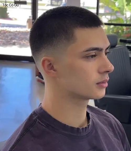 Một chàng trai trẻ với kiểu tóc buzz cut Mid Fade ngắn đều, được cạo sát một cách tinh tế và hiện đại, mang lại vẻ ngoài trẻ trung