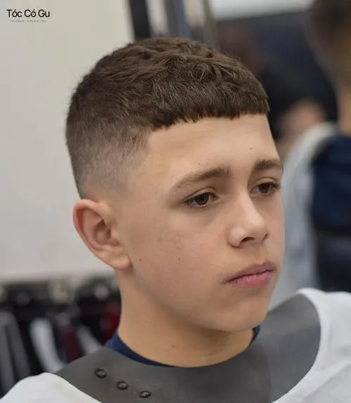 Nam thanh niên châu Á có mái tóc buzz cut sóng gợn nhỏ đen, ngắn, diện áo len xám cổ tròn
