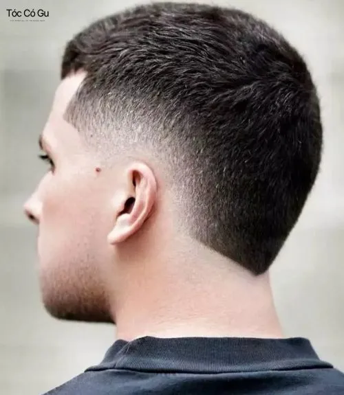 Góc nhìn nghiêng của người đàn ông với kiểu tóc Burst Fade + buzz cut gọn gàng. Phần gáy được tạo kiểu cắt vuông