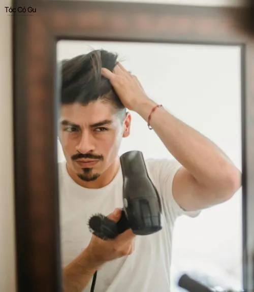 Tóc Side Part là gì? Top 10 kiểu tóc Side Part quốc dân hiện nay Nam giới dùng máy sấy và tay vuốt tóc Side Part trước gương.