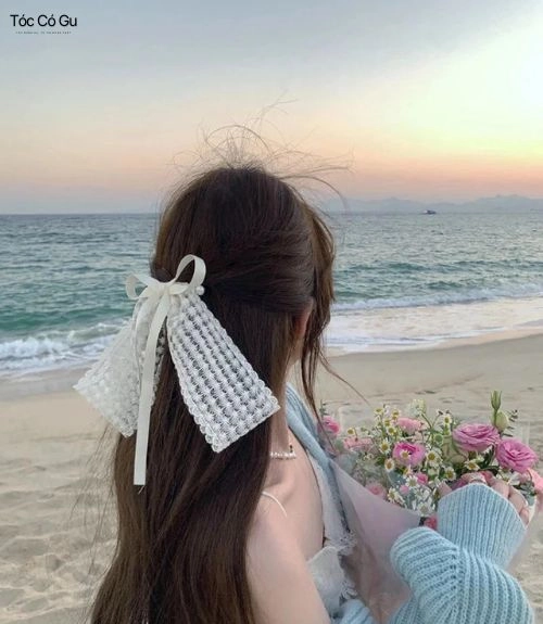 10+ kiểu tóc đi biển trẻ trung, giúp nàng nổi bật mọi khung hình Kiểu tóc buộc nửa đầu gắn nơ trắng tinh tế đứng trước sóng biển