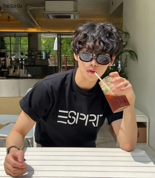 Hot boy đeo kính đen ngầu đang uống cà phê, nổi bật với kiểu tóc mì tôm nam uốn xoăn tít cá tính Hàn Quốc